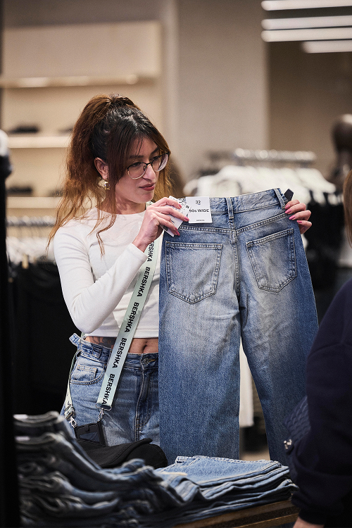 A sales assistant holds a pair of denim trousers while tyding a counter with folded jeans.