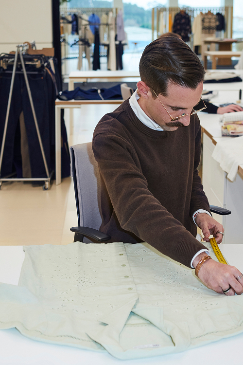 A Zara designer takes measurements of a button-down shirt on his desk with a tape measure.