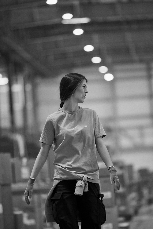 An employee at a Zara logistics platform smiles and walks through the aisles wearing work gloves