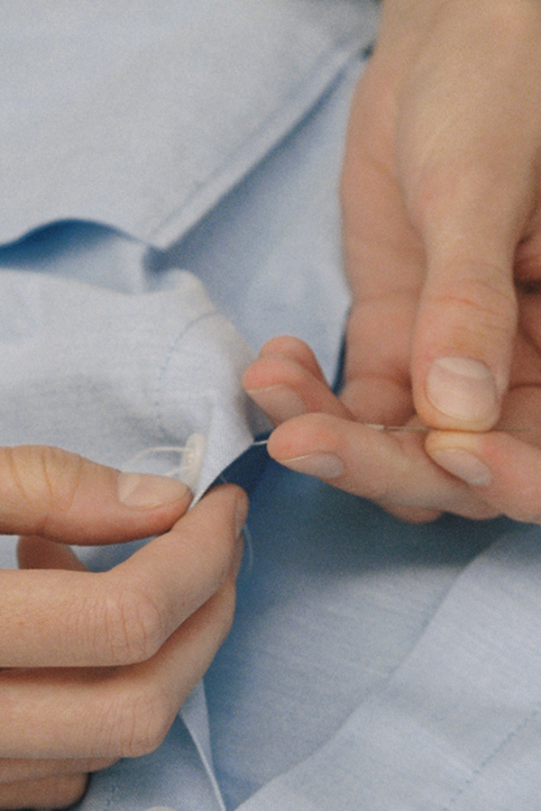 Detail of hands sewing a button on a shirt