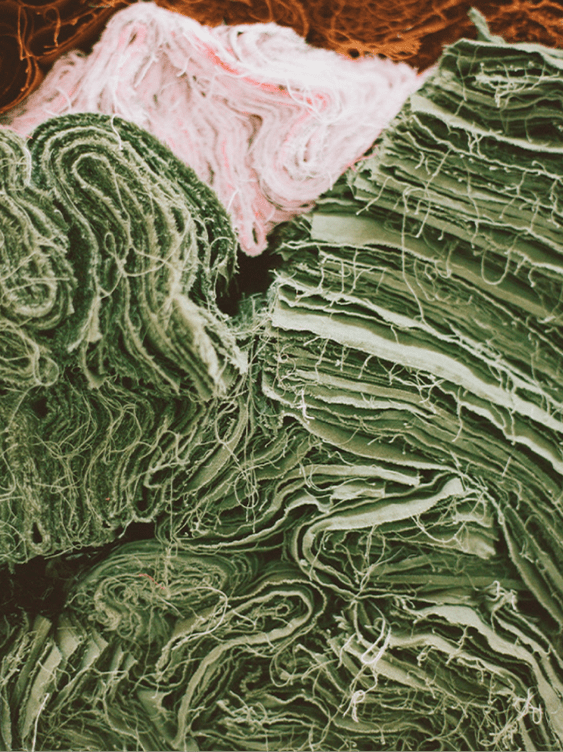 Piles of scraps of green and pink fabric with loose threads.