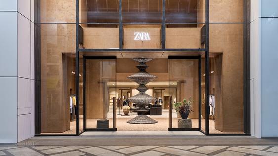 Facade of a Zara store with a large glass display window, neon logo and a woven sculpture in the center.