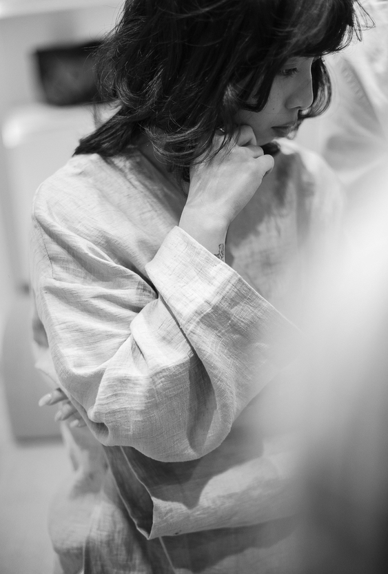 Black and white portrait of a thoughtful woman with dark hair and a linen shirt, with her hand on her chin.