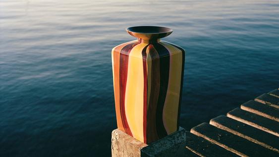 Large, tall, rectangular vase with colored stripes, placed on a pier pillar by the sea.