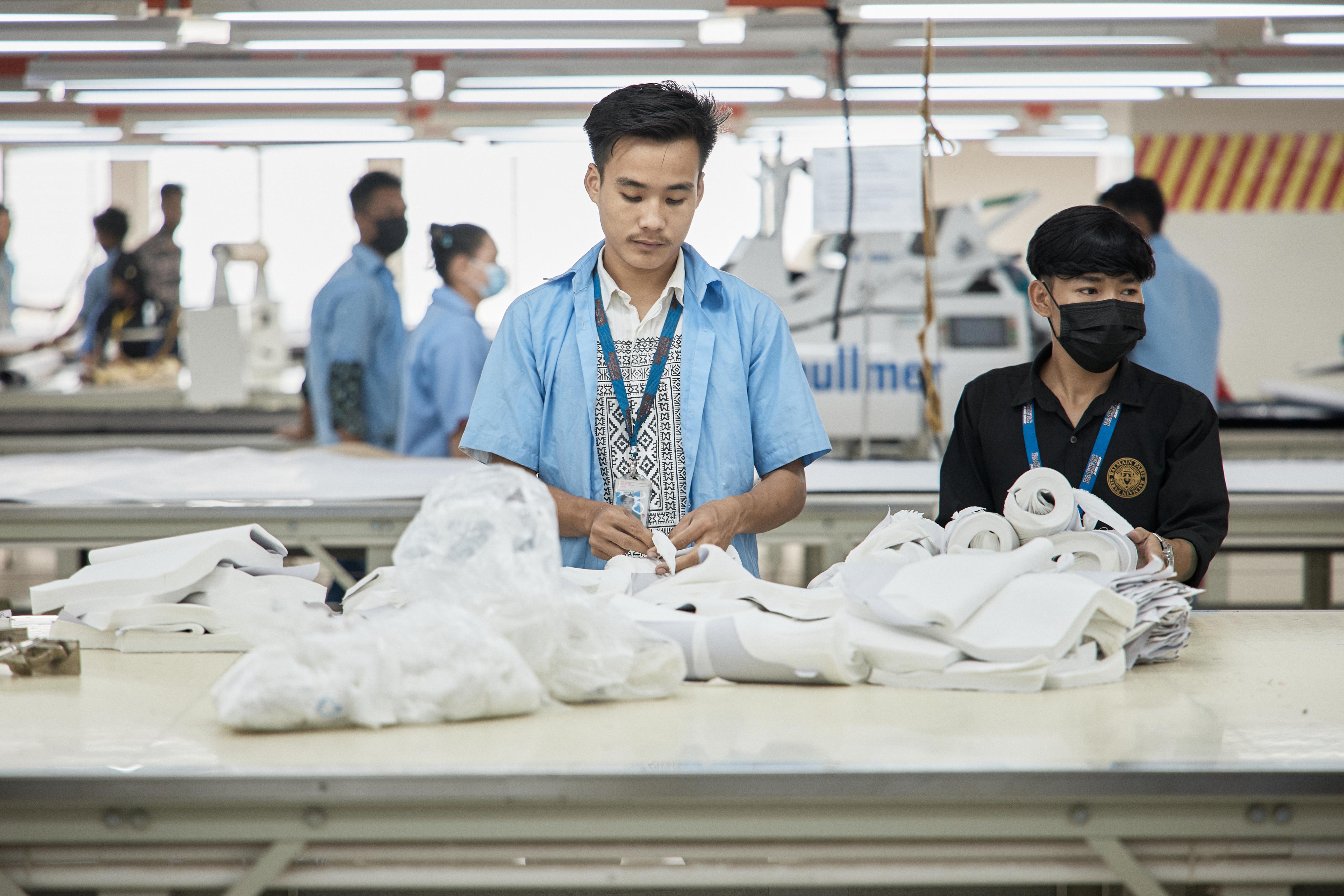 Two men working with white fabrics at a counter in a textile factory.