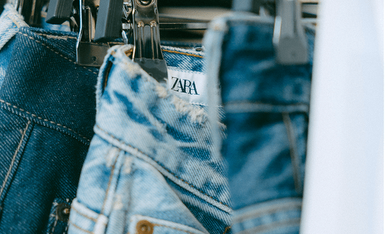 Jeans with the Zara brand label hanging on a clothes rack.