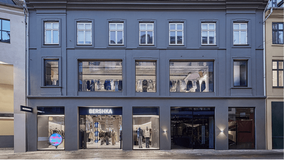 Exterior of a Bershka store in a gray building with large shop windows and clothes on display.