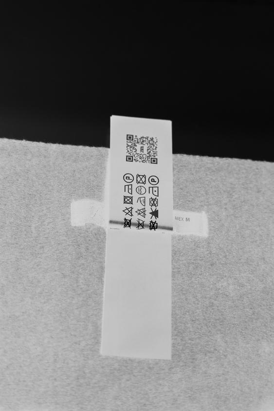 Clothing label with care symbols and QR code on gray fabric.