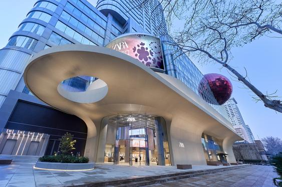 Modern entrance of a Zara store with a curved canopy, a digital screen and a decorative pink sphere.