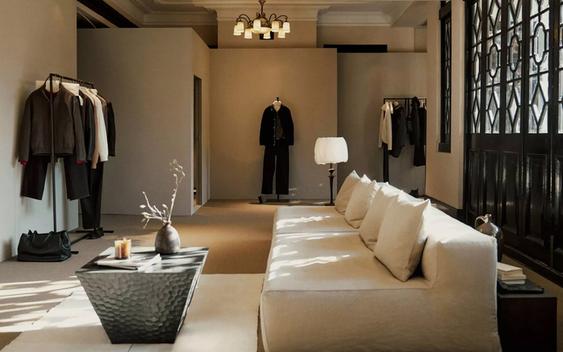 A minimalist fashion showroom with Massimo Dutti clothing on racks and mannequins. There's a light-colored sofa and natural light.