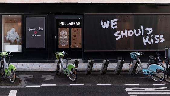 Exterior of a Pull&Bear store with rental bikes parked on the street and a sign that says "WE SHOULD KISS".