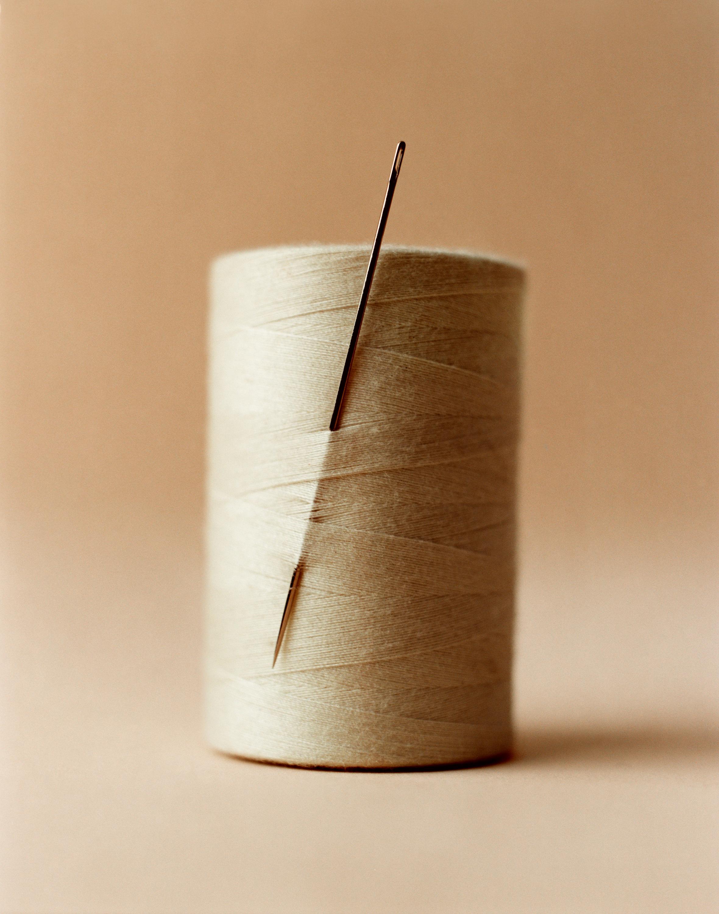Sewing needle stuck in a spool of beige thread.