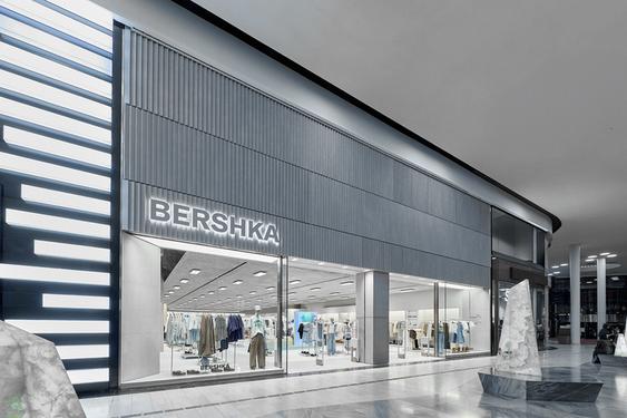Modern facade of a Bershka store with illuminated logo and shop windows displaying clothing.