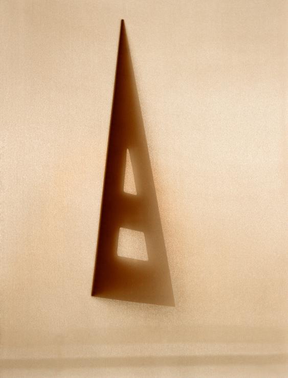 Shadow of a triangular ruler with geometric cutouts on a textured light brown surface.