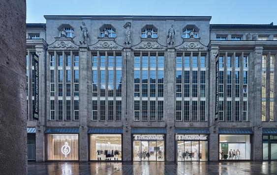 Ornate facade of a stone building with Stradivarius shops on the ground floor.