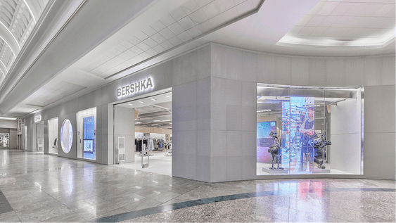 Exterior de una tienda Bershka moderna en un centro comercial, con escaparates digitales y un pasillo vacío.