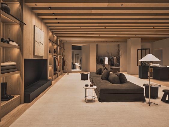 Modern shop interior with wooden ceiling, illuminated shelves and a gray sofa.
